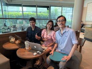 3 คนนั่งที่โต๊ะกลมในร้านกาแฟพร้อมแล็ปท็อป