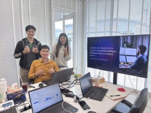 ผู้เรียนนั่งเรียนที่โต๊ะพร้อมแล็ปท็อปและจอสไลด์ในห้องประชุม