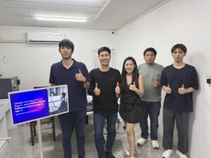 ภาพหมู่ผู้เรียน 6 คนชูนิ้วโป้งข้างจอแสดงสไลด์ในห้องอบรม